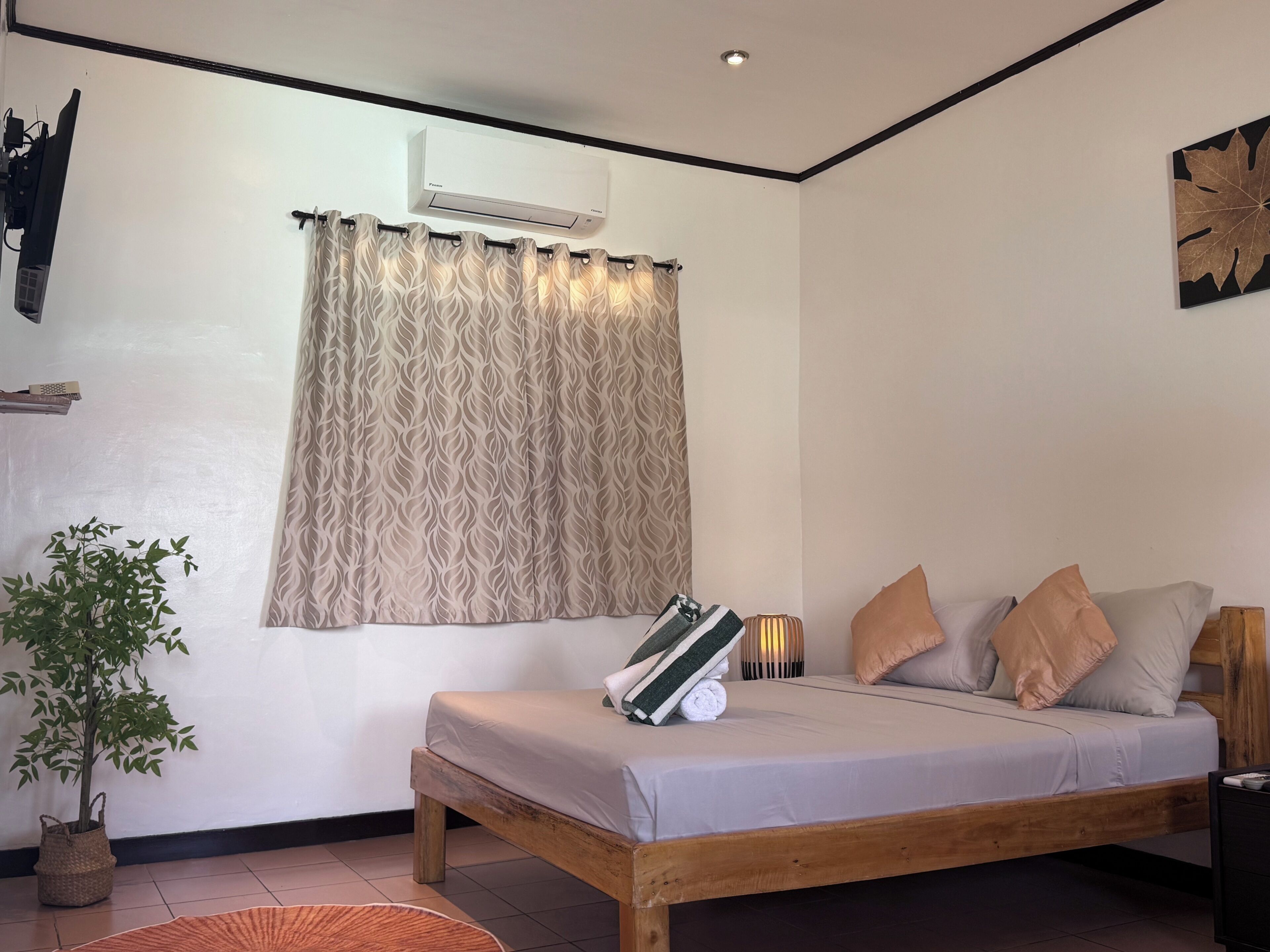 A bedroom with a bed, a potted plant, an air conditioning unit, and a wall-mounted shelf.