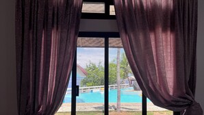 Una ventana con cortinas y vistas a una piscina, además de un edificio con techo rojo.
