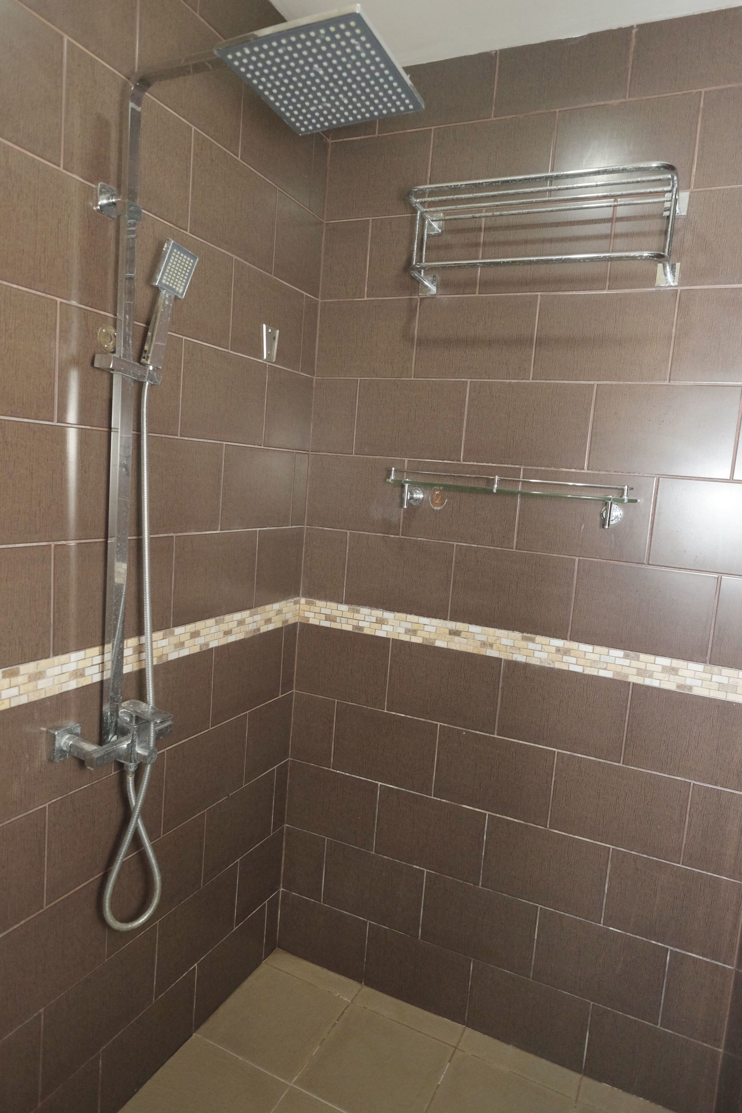 A shower with a handheld showerhead and a fixed showerhead, a towel rack, and a tiled floor.