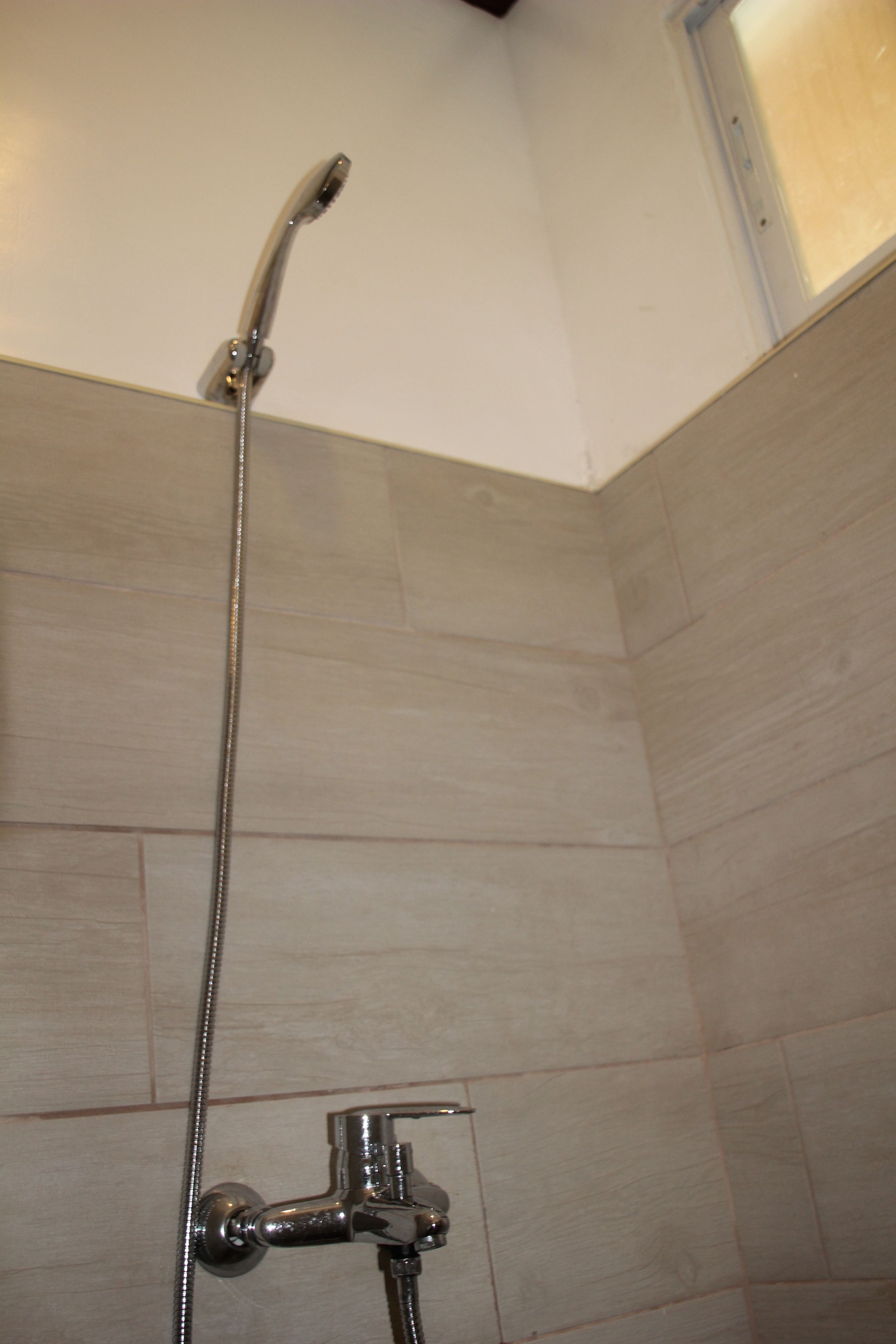 A shower with a handheld showerhead and a wall-mounted faucet.