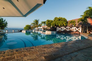 A swimming pool with a stone deck, palm trees, and a view of the ocean.