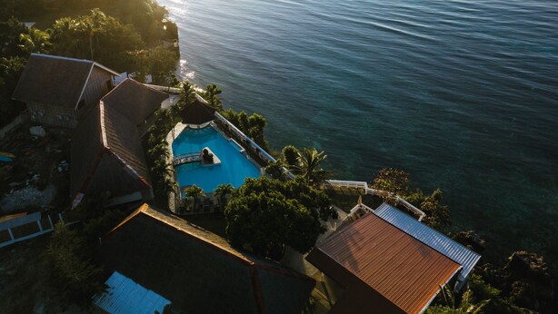 Vista aérea de un resort con piscina rodeada de palmeras y vista al mar.