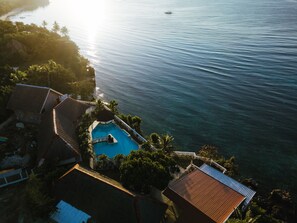 Vista aérea de un resort con piscina rodeada de palmeras y vista al mar.