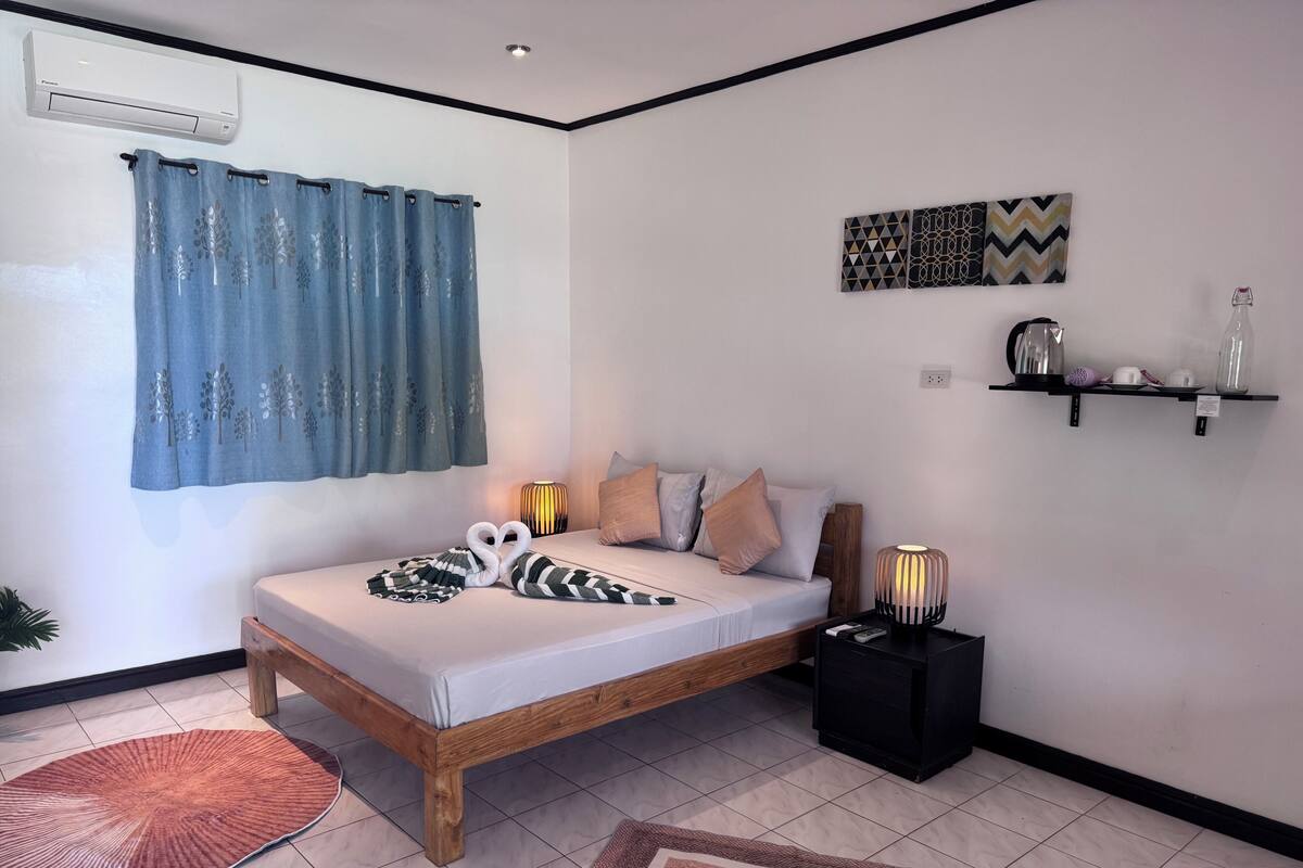 Un dormitorio ordenado con cama, lámparas de noche, una repisa con utensilios de cocina y un aire acondicionado instalado en la pared.