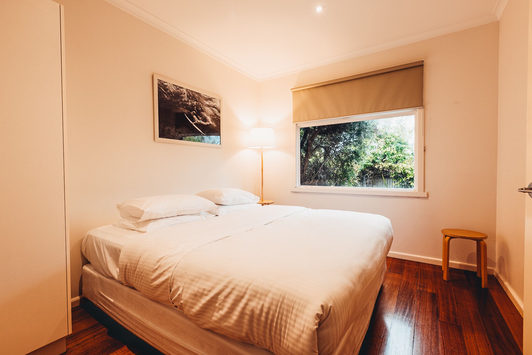 Una camera da letto con un letto, una finestra vista alberi, una lampada e uno sgabello.