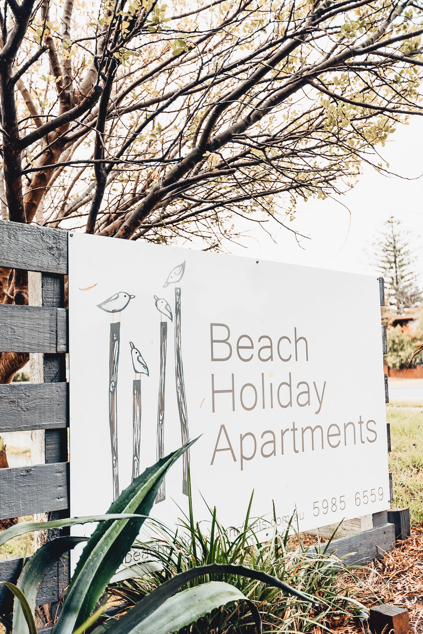 A sign for Beach Holiday Apartments with a contact number.