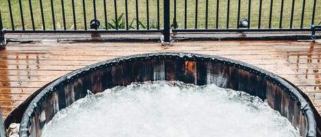 Un jacuzzi en una terraza de madera con una valla metálica al fondo.