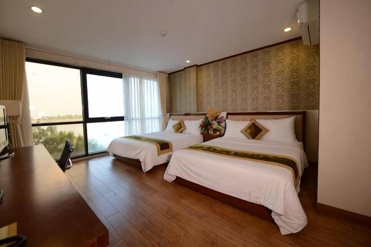 Habitación de hotel con dos camas, un escritorio y un ventanal grande.