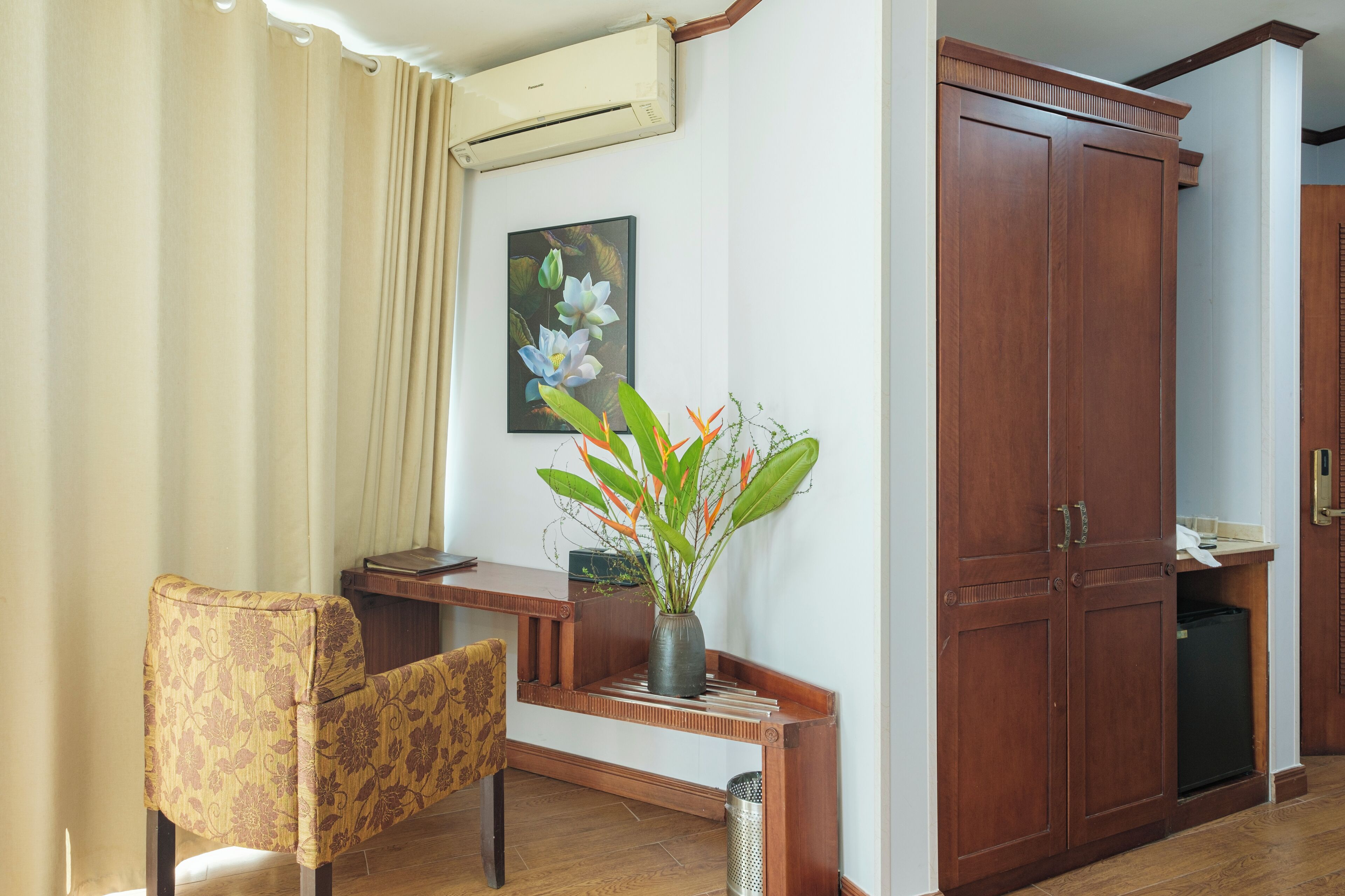 A room with a wooden desk, a chair, a large wardrobe, and a wall-mounted air conditioner.