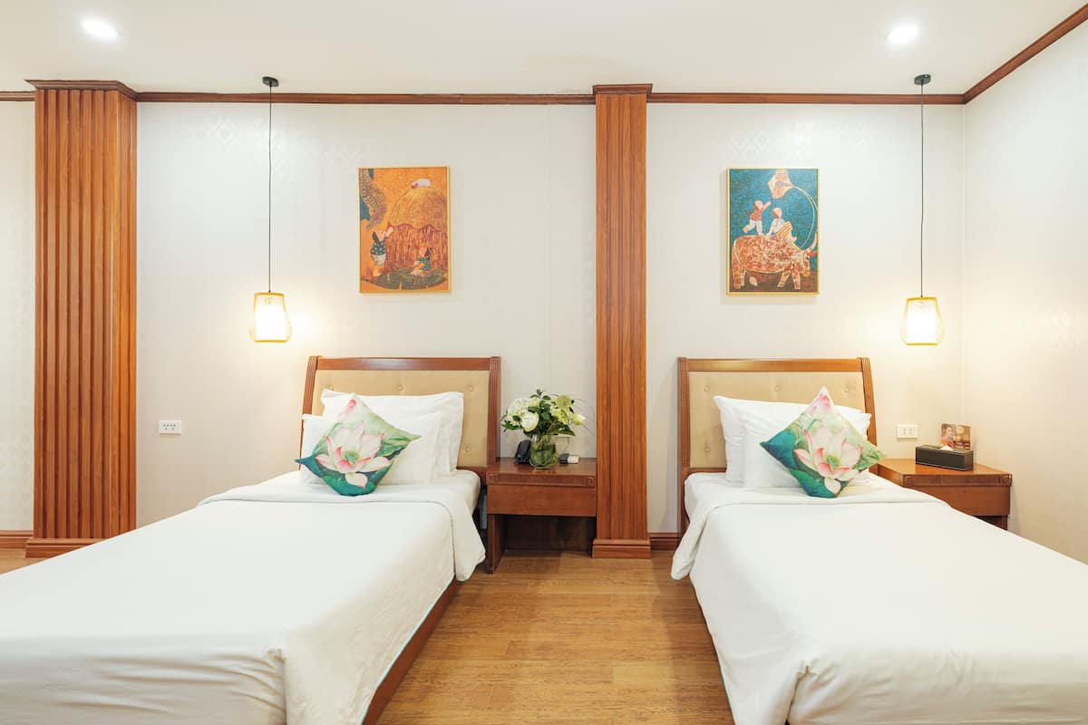 Habitación de hotel con dos camas, cabeceros de madera y mesitas de noche con lámparas.