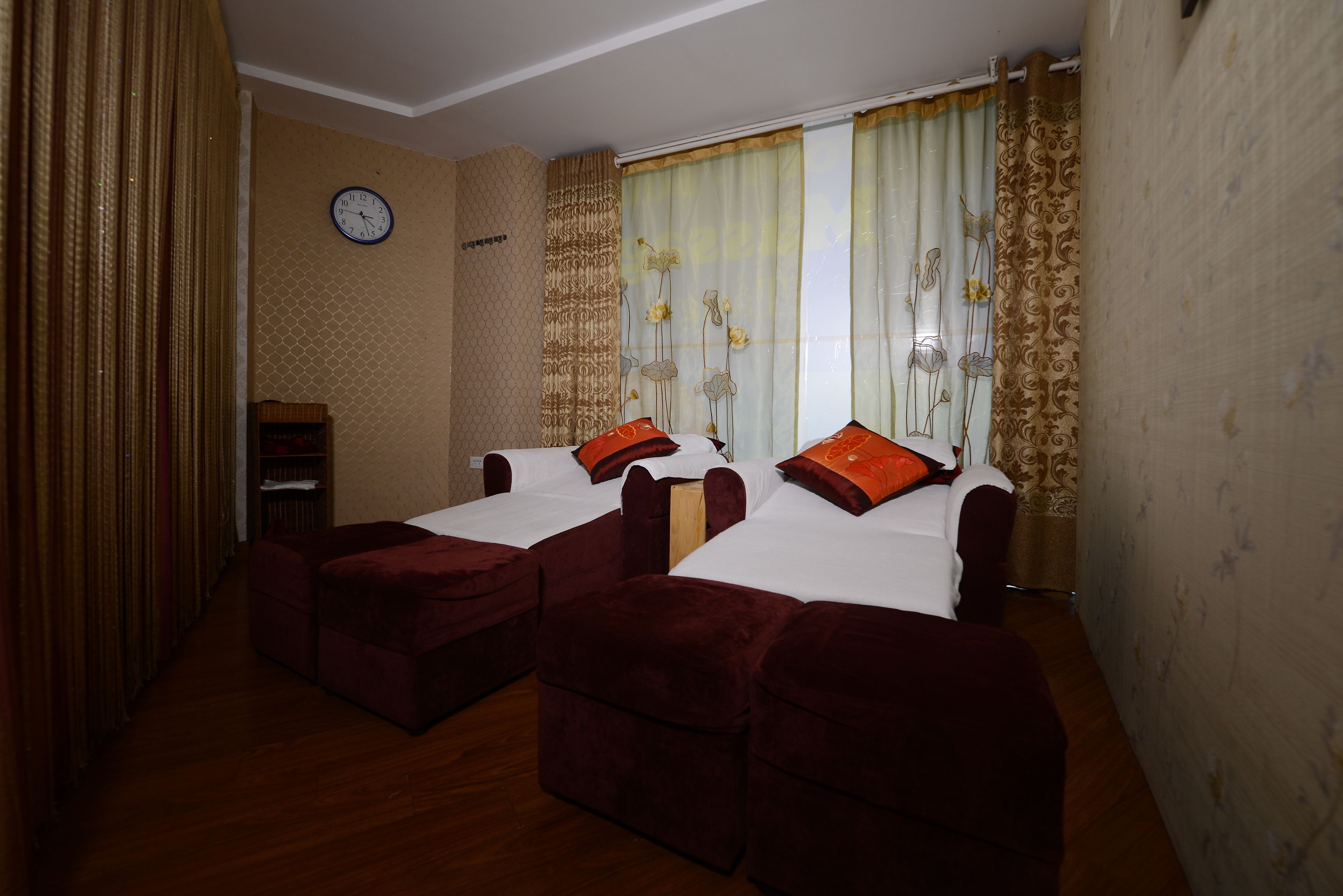 A hotel room with two beds, a clock on the wall, and a window with curtains.