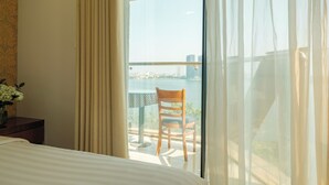 Una habitación de hotel con una cama, una mesita con mantel a cuadros, un florero con flores y vistas a un balcón con una silla y una mesa.