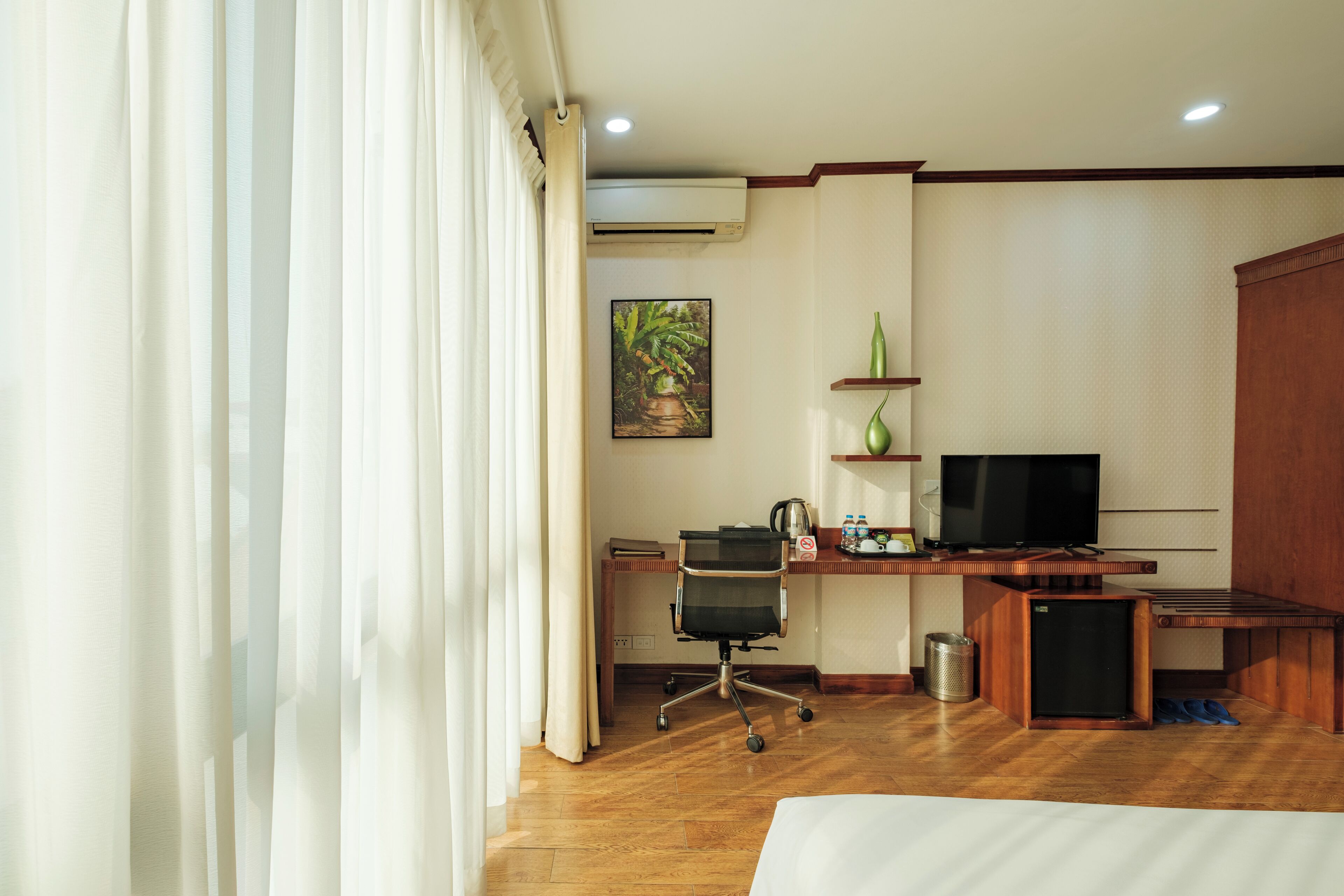 Ein Hotelzimmer mit einem Holztisch, einem Fernseher, einem Bett und einem Fenster mit Vorhängen.