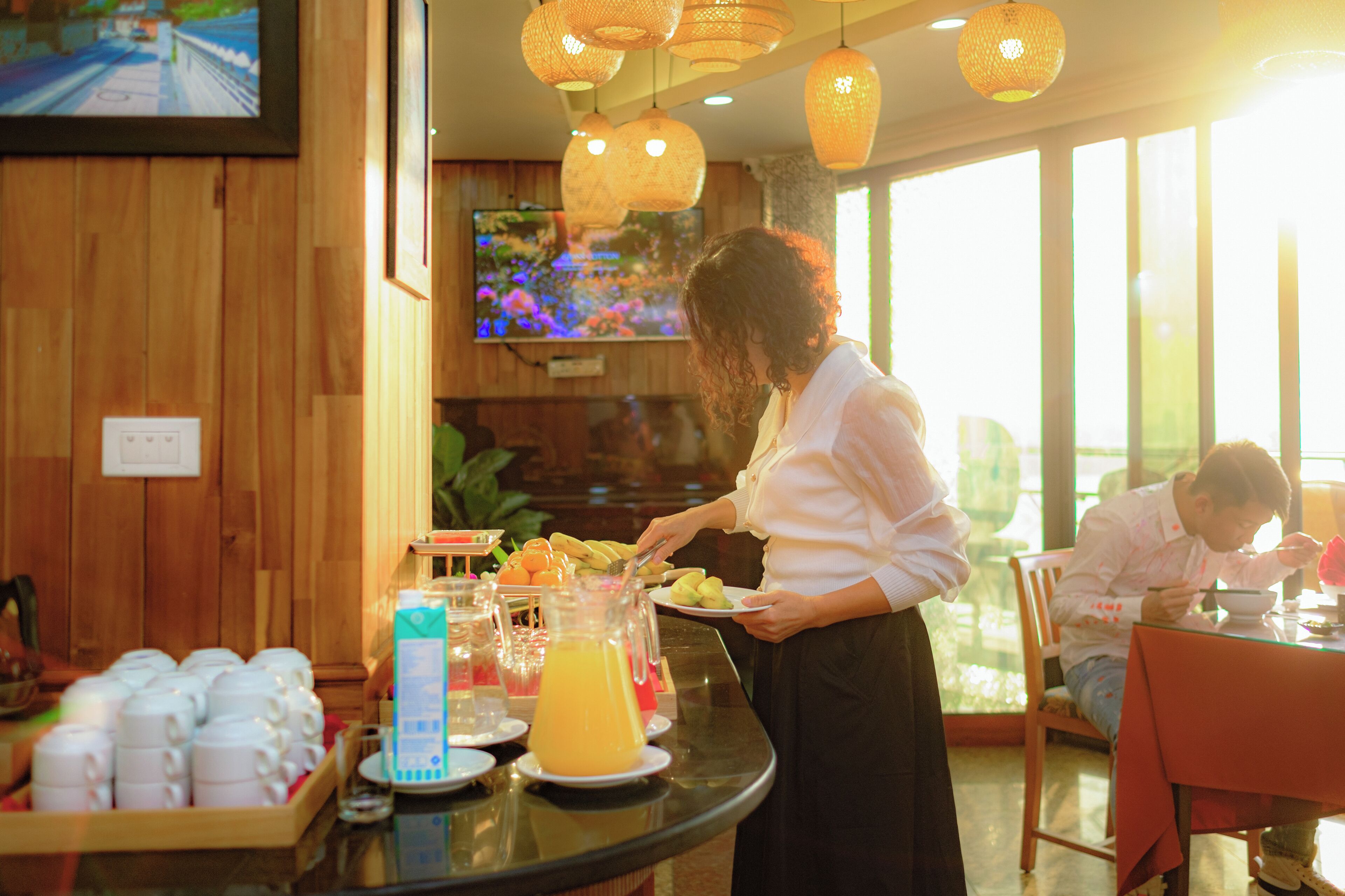 A breakfast buffet with a variety of fruits and beverages, a television mounted on the wall, and a wooden interior.