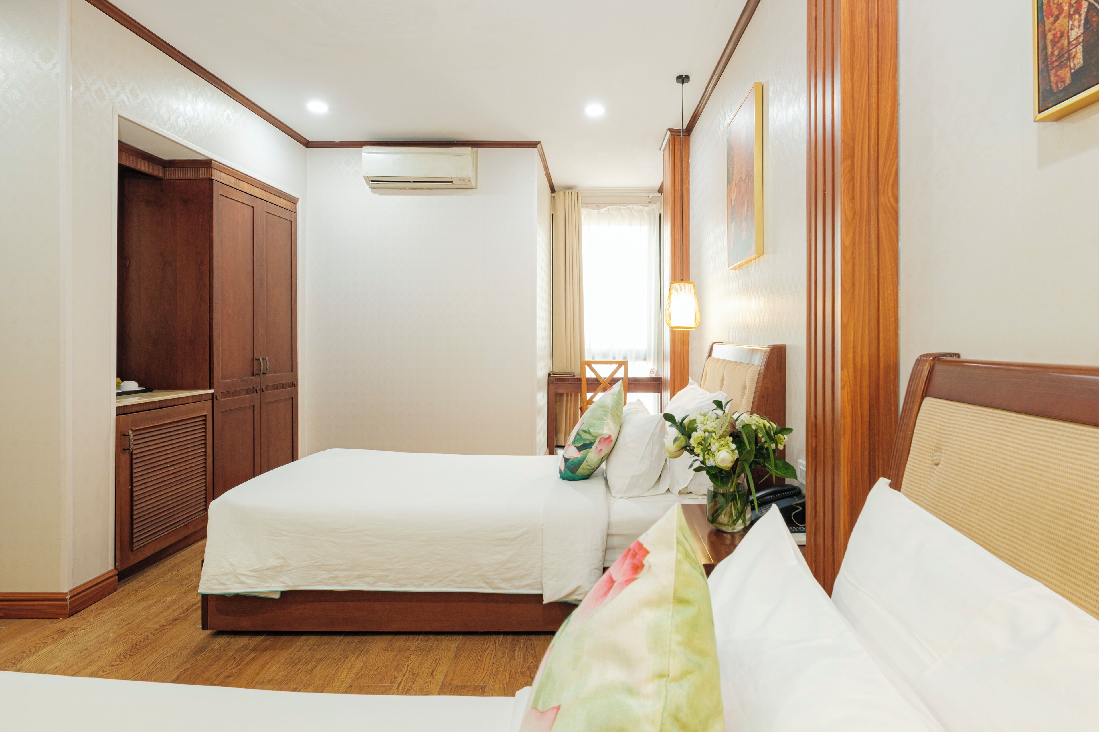 Une chambre d’hôtel avec deux lits, une armoire, un bureau avec une lampe et une fenêtre avec des rideaux.