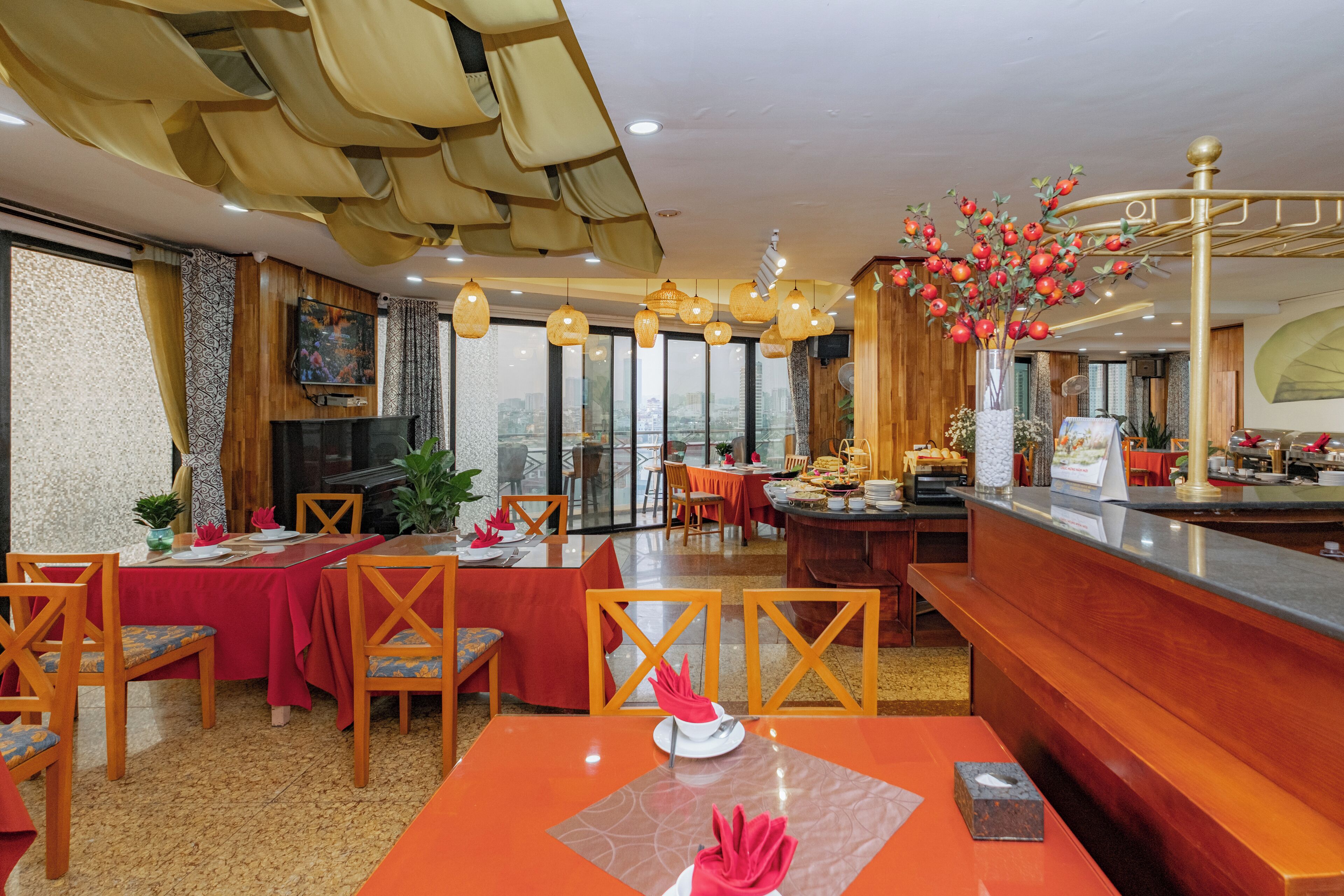 Un comedor de hotel con mesas dispuestas para los huéspedes, una recepción y vistas de la ciudad a través de amplias ventanas.