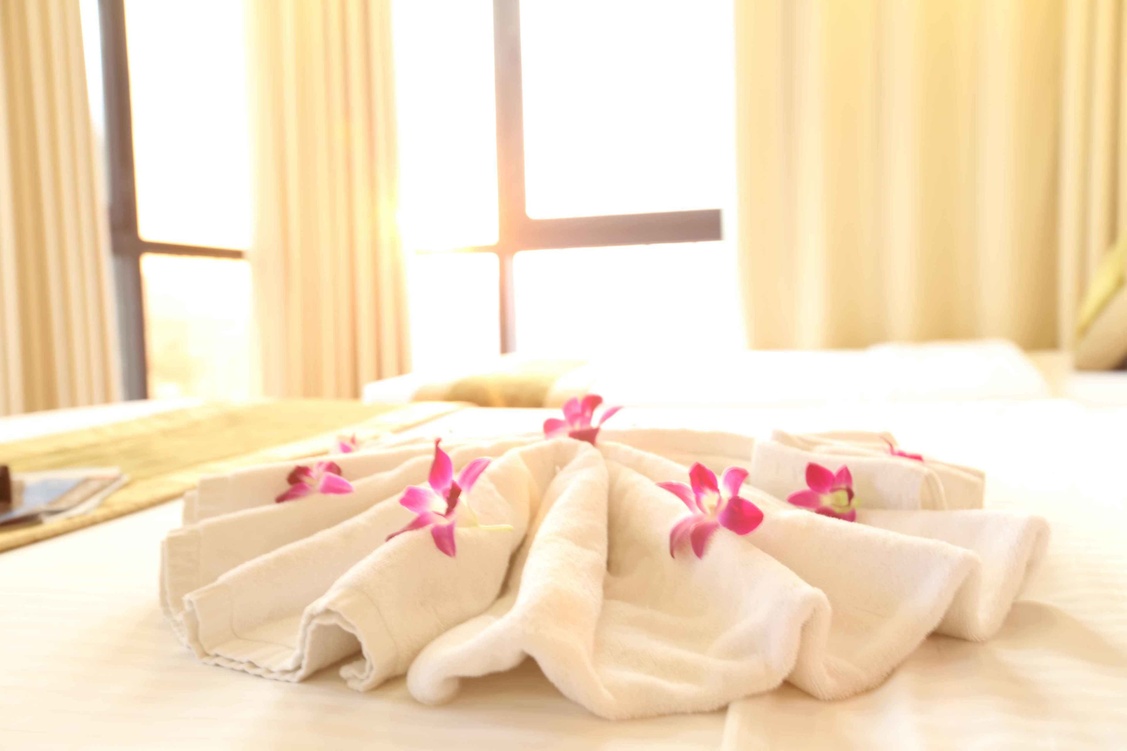 A neatly arranged set of towels with pink flowers on a bed, with a window and curtains in the background.