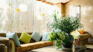 Un salón bien iluminado con sofá, cojines, una mesa de centro y un jarrón con flores.