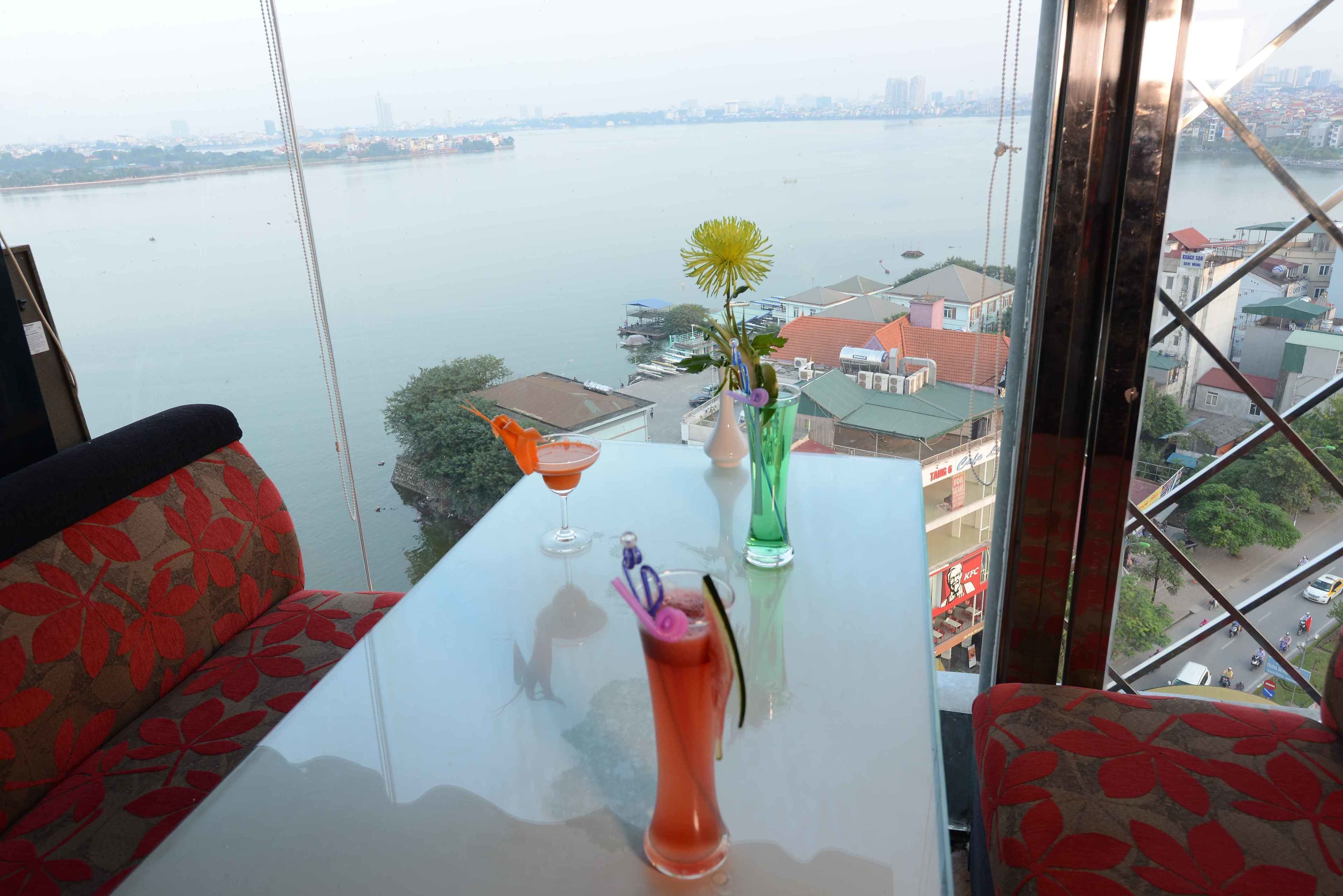 A table with a drink, a vase with a flower, and a view of a river and cityscape.