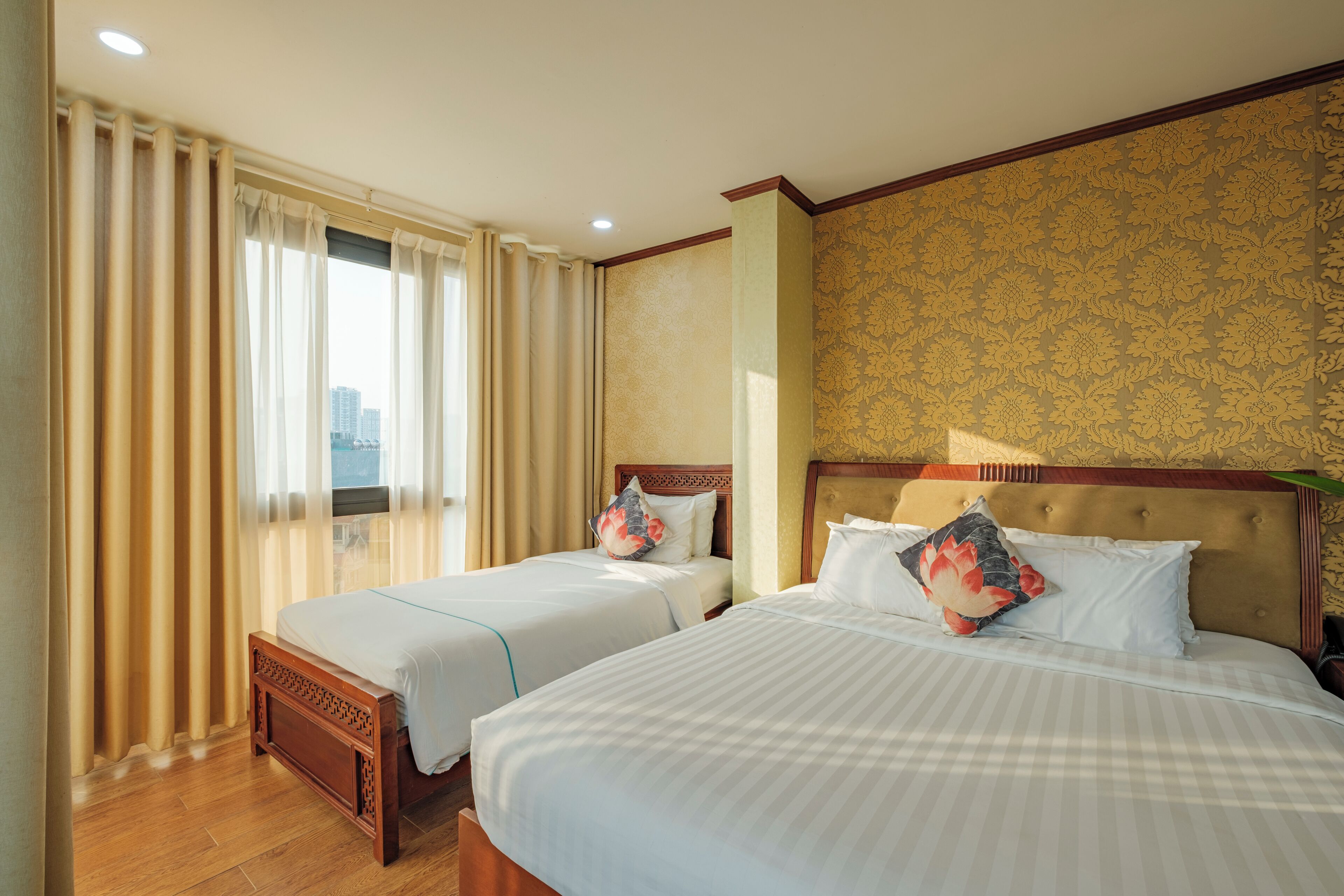 Une chambre d’hôtel avec deux lits, une grande fenêtre avec des rideaux et un mur décoré d’un motif.