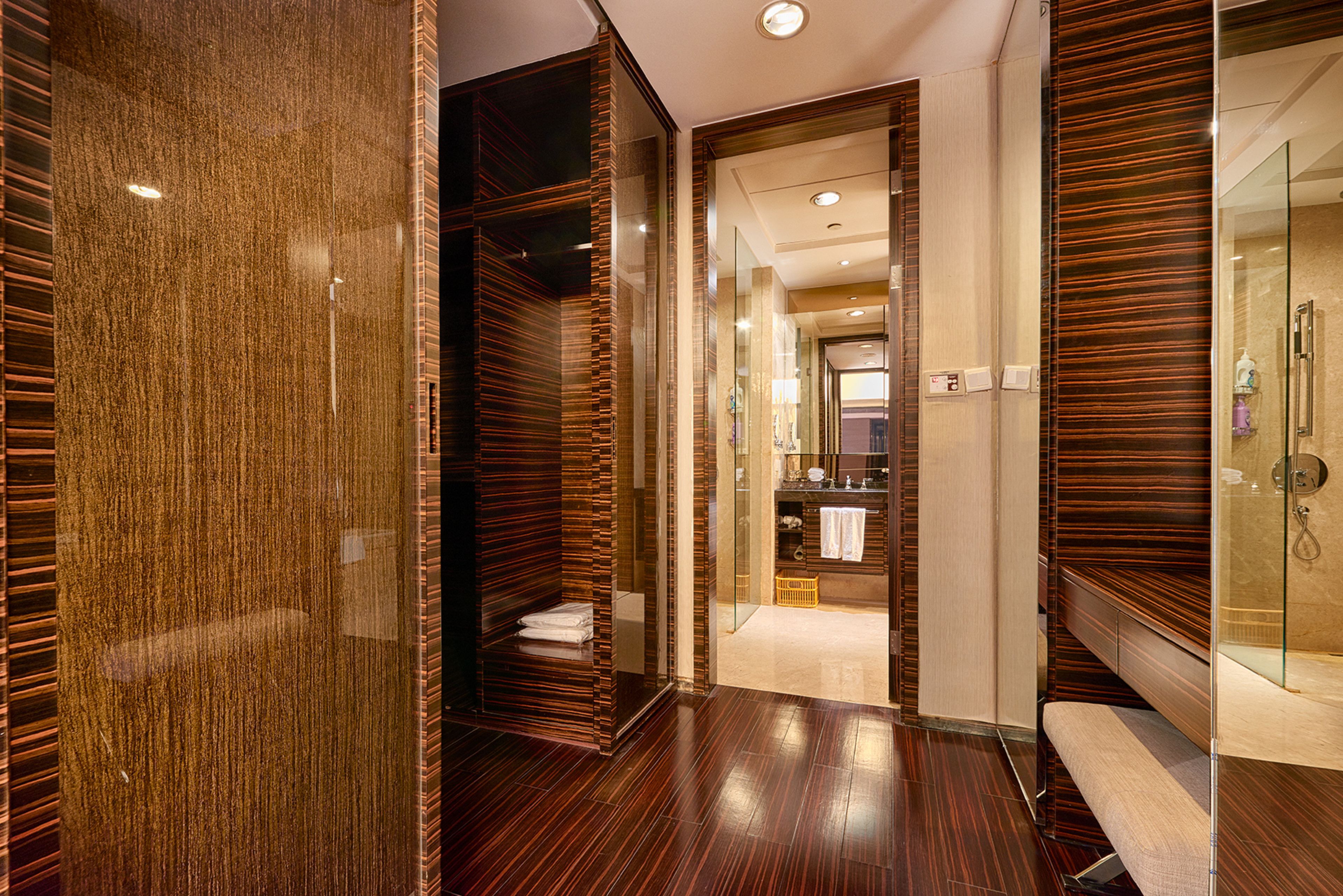 A modern hotel corridor with wooden paneling, a glass-enclosed shower area, and a visible bathroom with a towel rack.