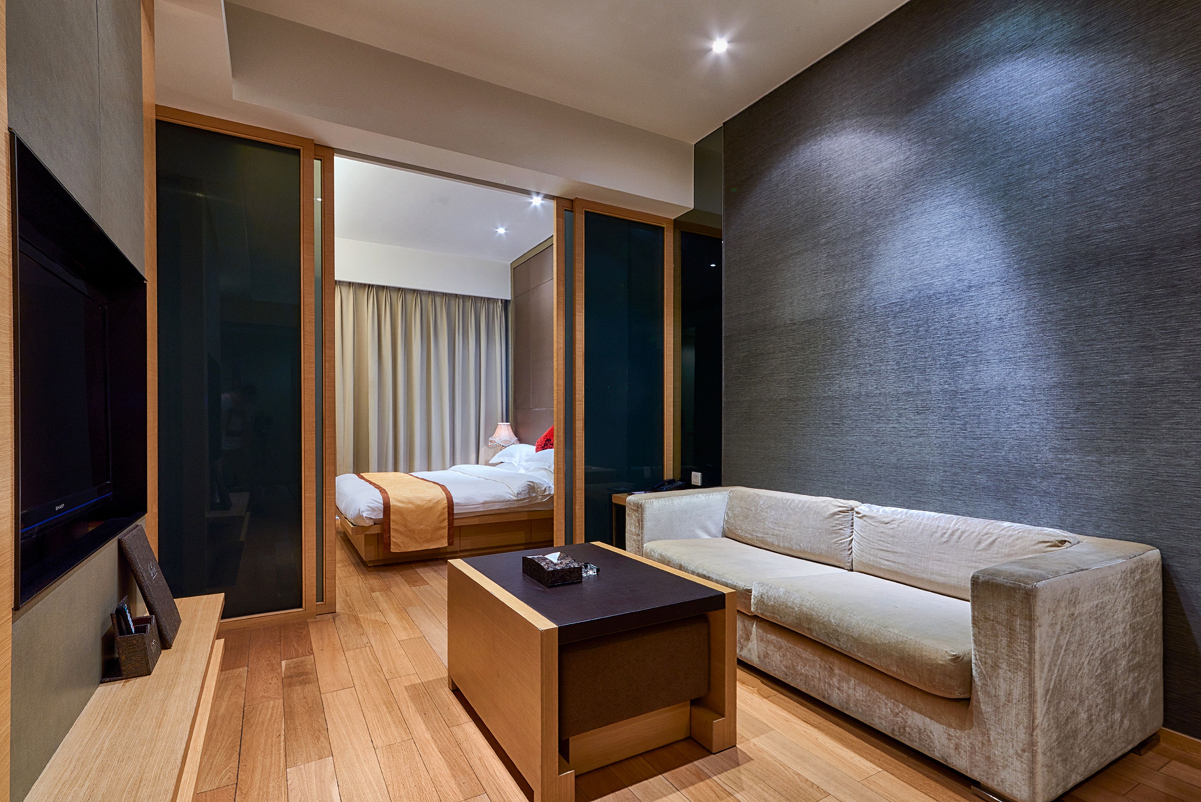 A modern hotel room with a wooden floor, a sofa, a small table, a bed with a curtain, and a TV.