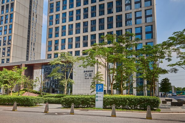 Un edificio moderno con un letrero de estacionamiento, rodeado de vegetación e infraestructura urbana.
