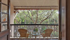 Un balcon ouvert donnant sur un jardin luxuriant, avec deux fauteuils en osier et une petite table.