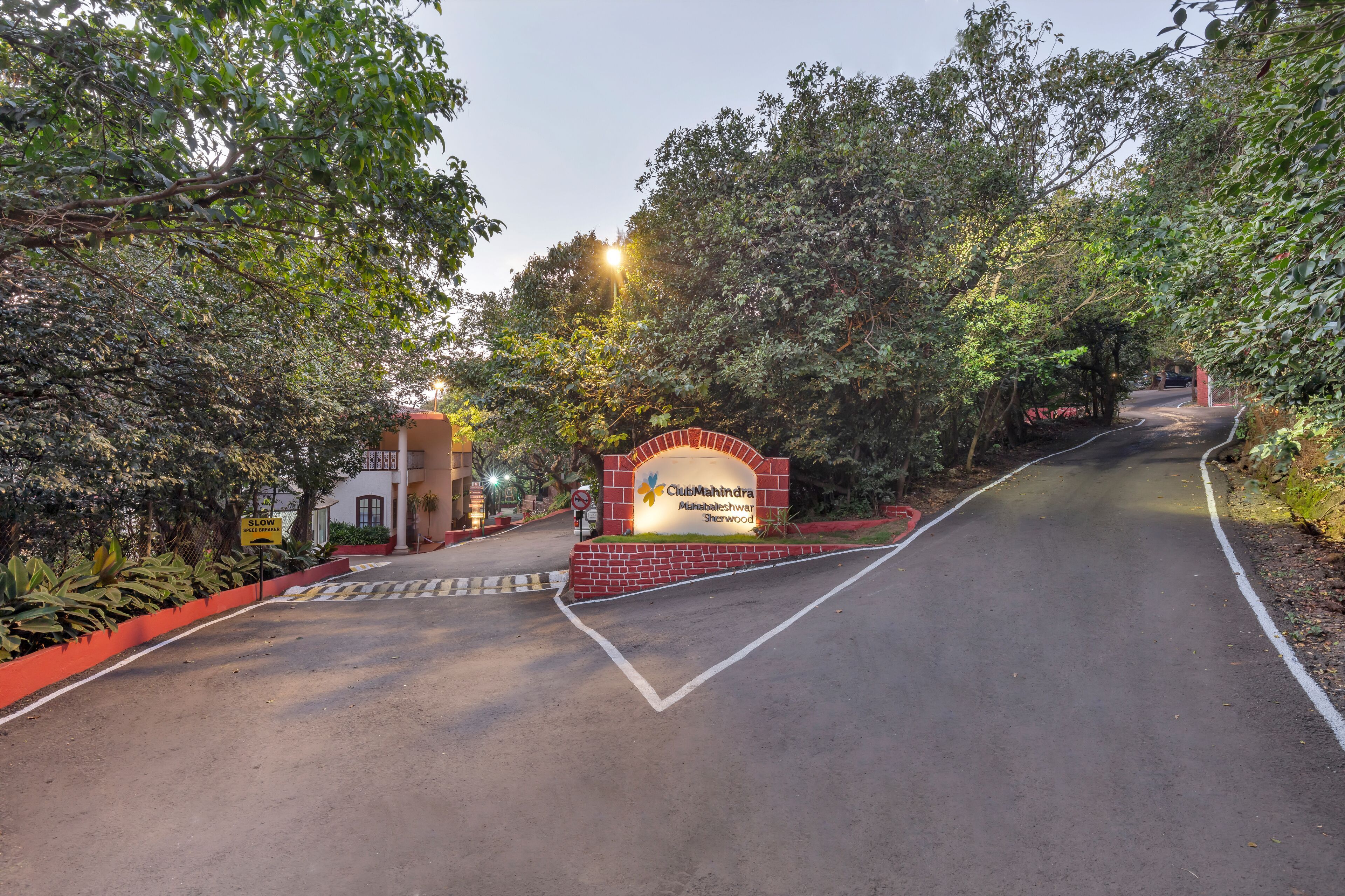 A road leading to a ClubMahindra property with a brick entrance and greenery on both sides.