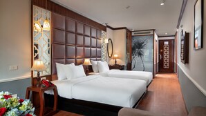 Habitación de hotel con dos camas, cabecera de madera, mesita de noche con lámpara, teléfono rojo y un jarrón con flores.