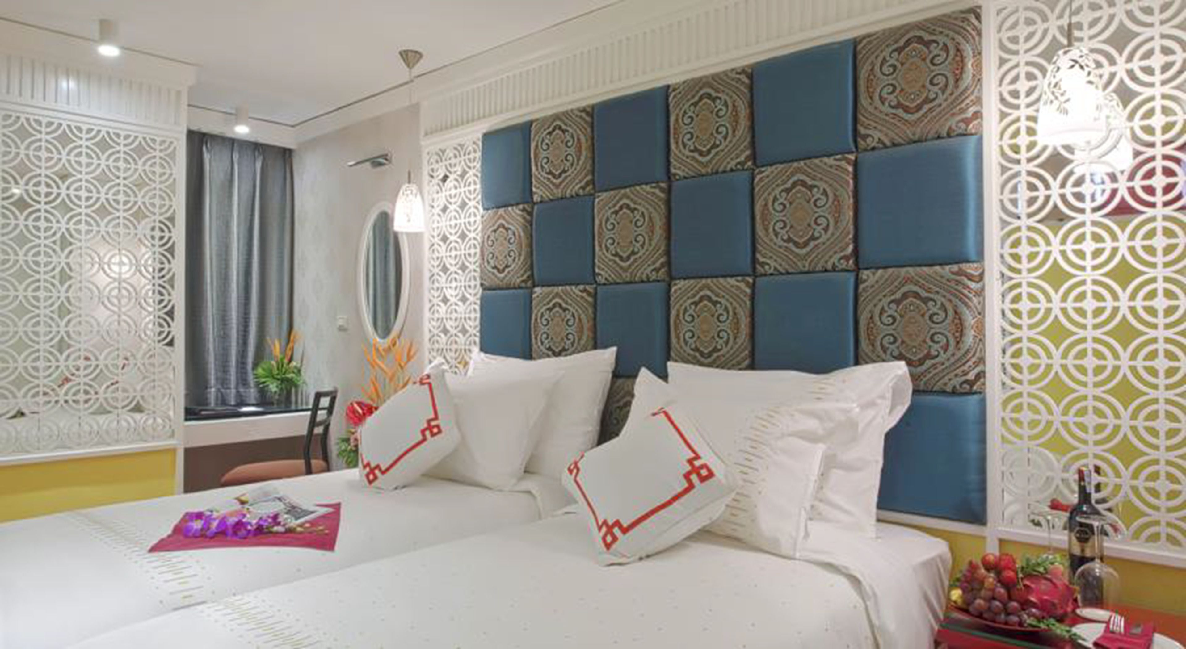 Een hotelkamer met een groot bed, een nachtkastje met een schaal fruit en decoratieve wandpanelen.