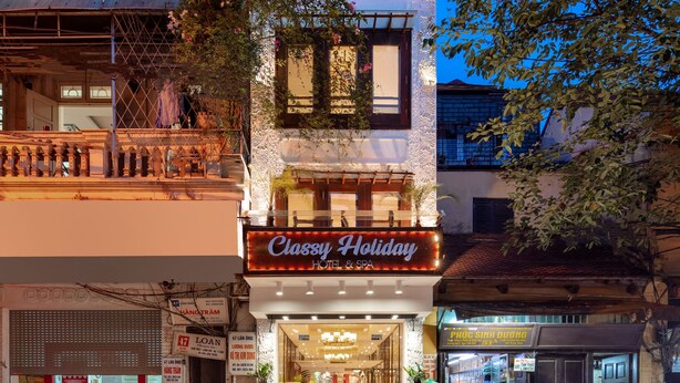 Un hotel con balcón, un cartel que dice 'Classy Holiday Hotel' y un escaparate con diversos artículos a la vista.