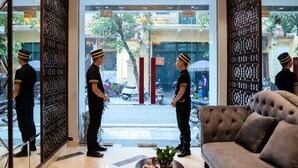 Vestíbulo de hotel con un sofá, paneles decorativos y dos empleados uniformados junto a la entrada.