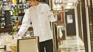 Un pasillo de hotel con un camarero llevando una bandeja de copas de vino.