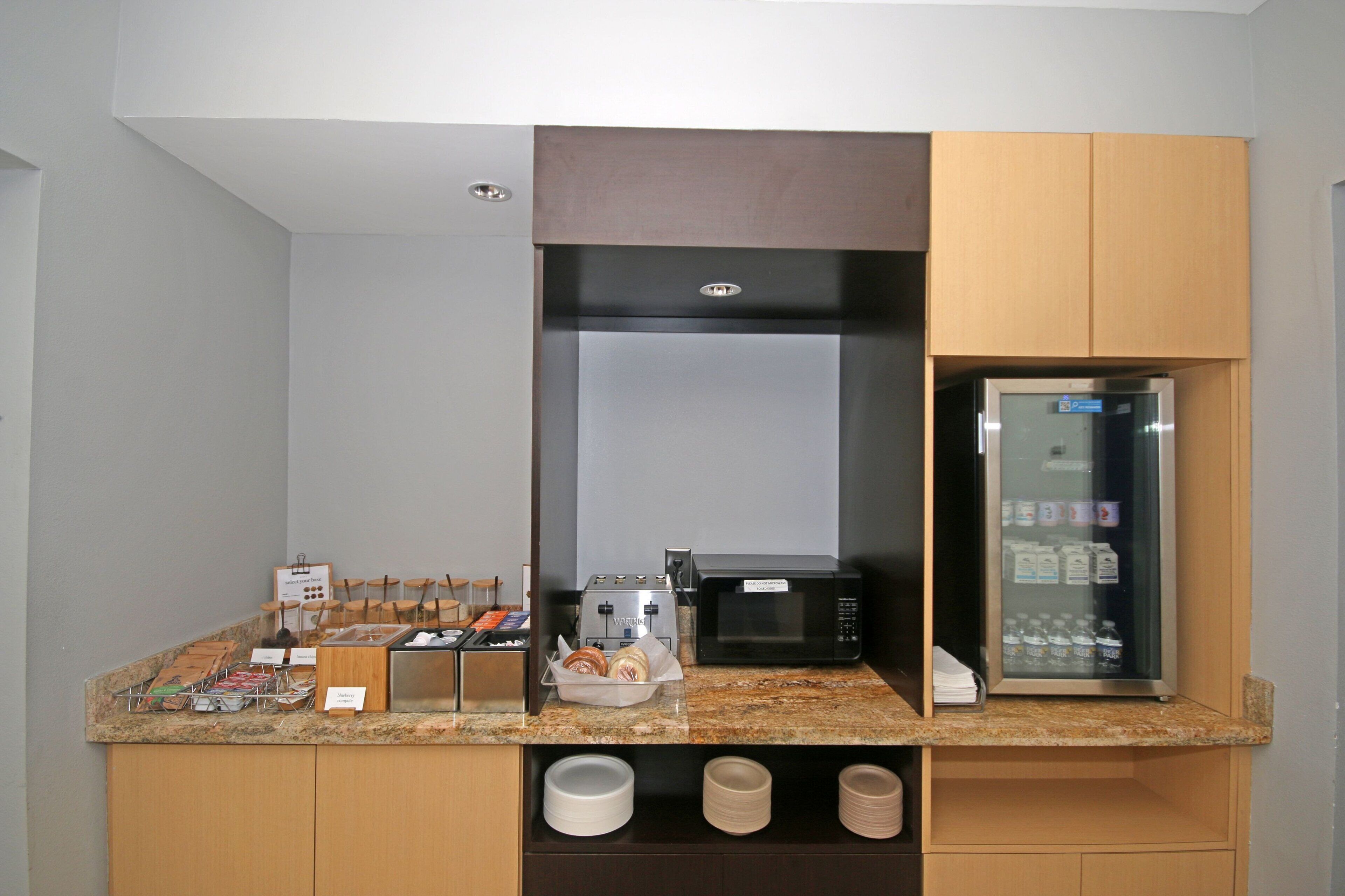 A kitchenette with a microwave, toaster, and refrigerator. There are utensils and plates on the counter.