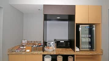 A kitchenette with a microwave, toaster, and refrigerator. There are utensils and plates on the counter.