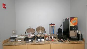A buffet setup with a coffee machine, a refrigerator, and various food containers.