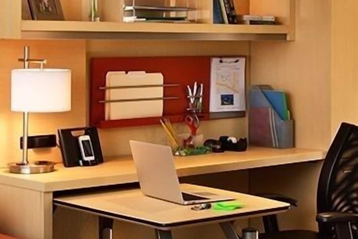 Ein Hotelzimmer mit Schreibtisch, Stuhl und einem Laptop. Auf dem Schreibtisch stehen eine Lampe, ein Telefon und eine Vase mit Blumen.