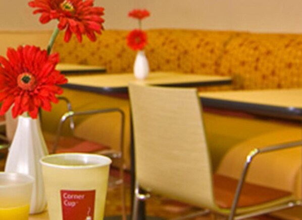 Un área de comedor con asientos tipo cabina amarillos, un jarrón blanco con flores rojas y una taza de café con la etiqueta 'Café Cup'.