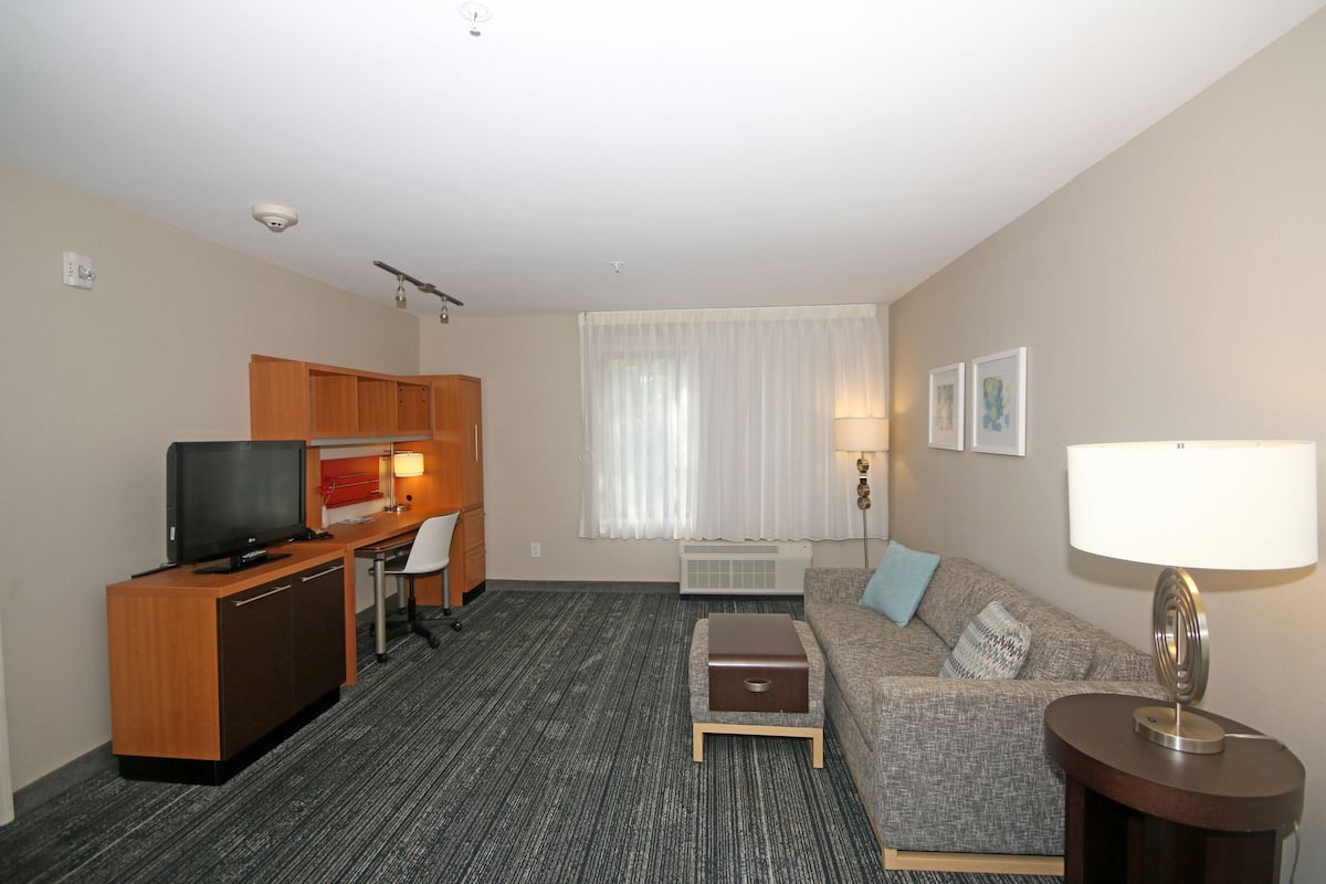 Ein Hotelzimmer mit Küchenzeile, einem Schreibtisch mit Stuhl, einer Couch, einer Lampe und einem Fernseher.