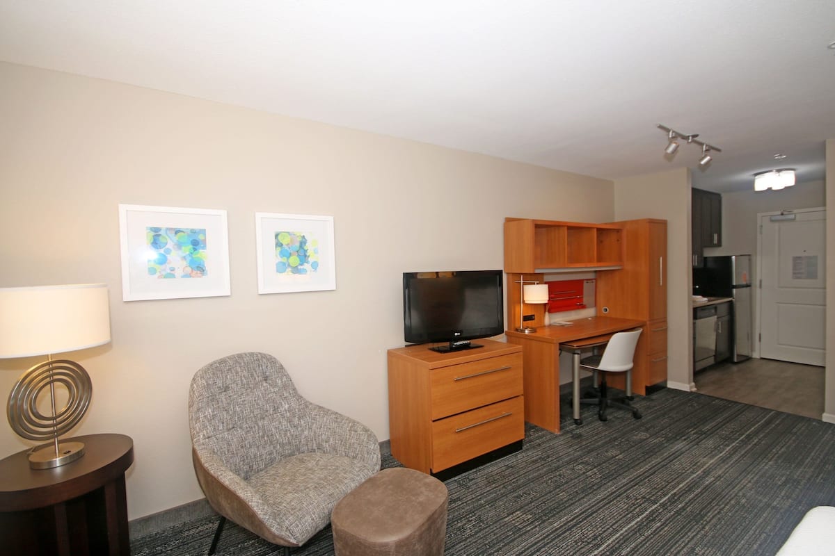 Ein Hotelzimmer mit Flachbildfernseher, Schreibtisch mit Stuhl, Sofa, kleinen Tisch mit Lampe und Wandbild.