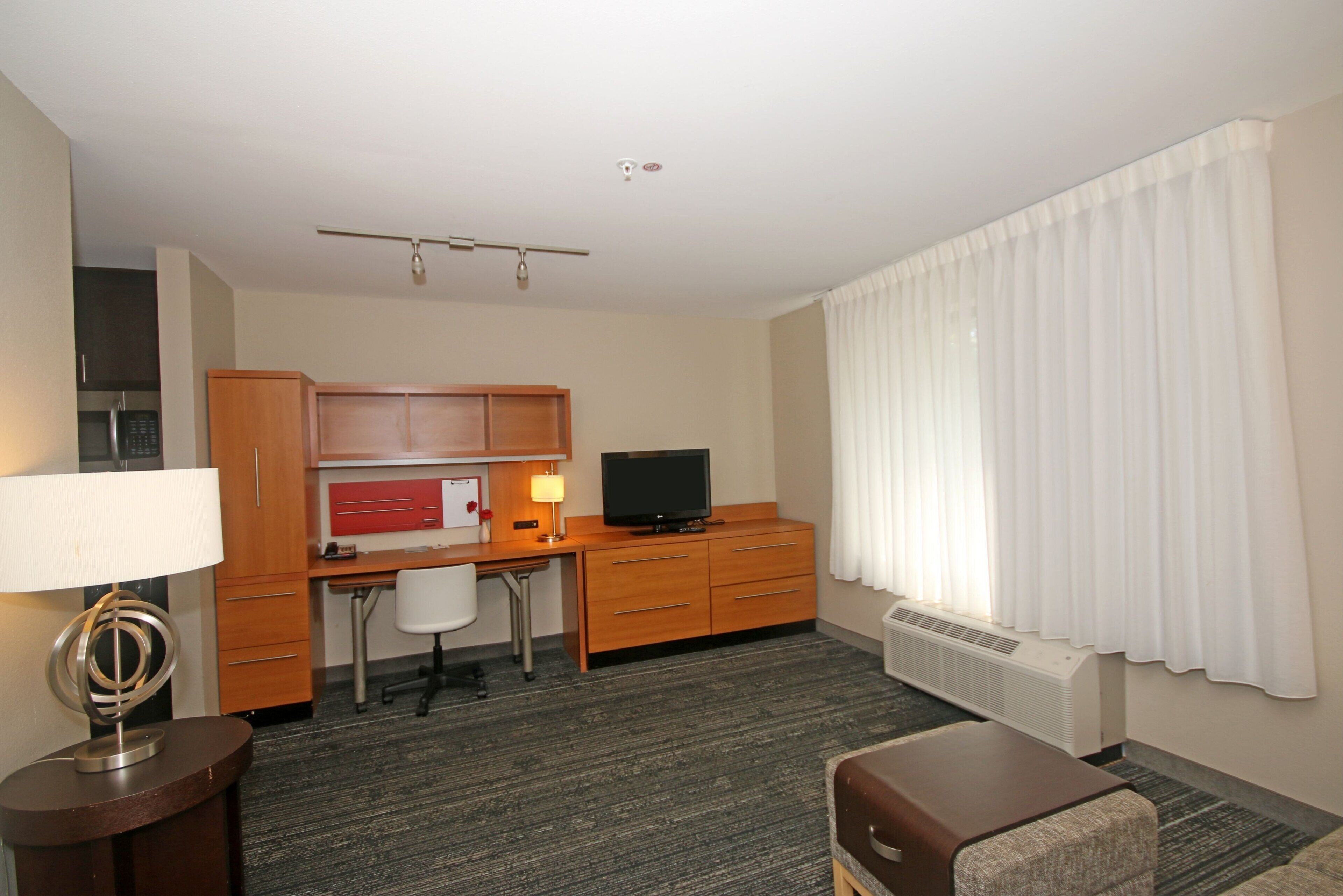 A hotel room with a desk, chair, television, and a small couch.