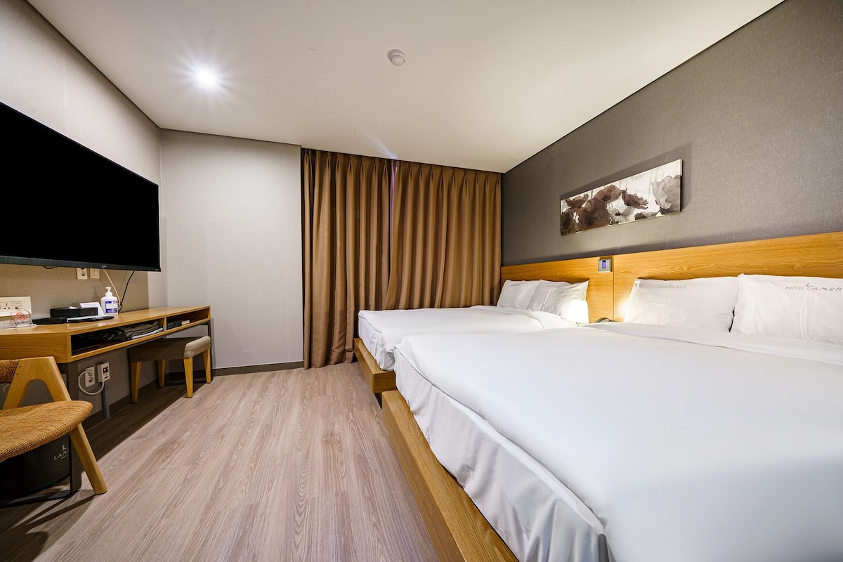 A hotel room with a large bed, a desk with a chair, a television, and a wall-mounted artwork.