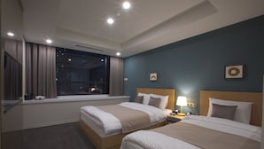 Une chambre d’hôtel avec deux lits, une fenêtre avec des rideaux, une table de chevet avec une lampe et un mur orné de tableaux.