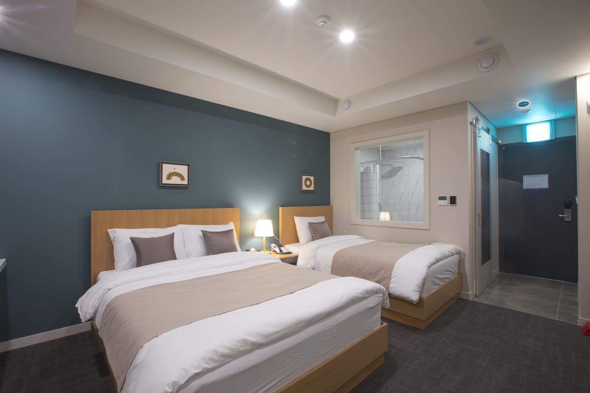 A hotel room with two beds, a window, and a door.