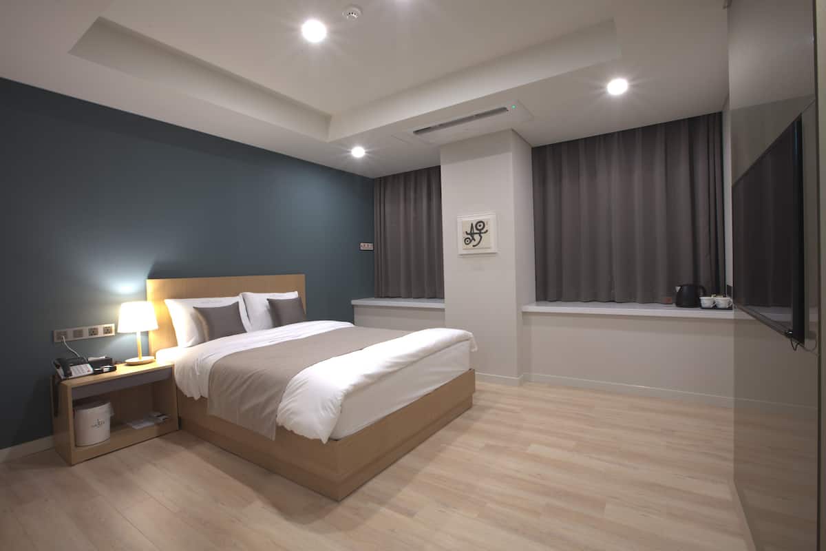 A modern bedroom with a bed, bedside table, lamp, and window with curtains.
