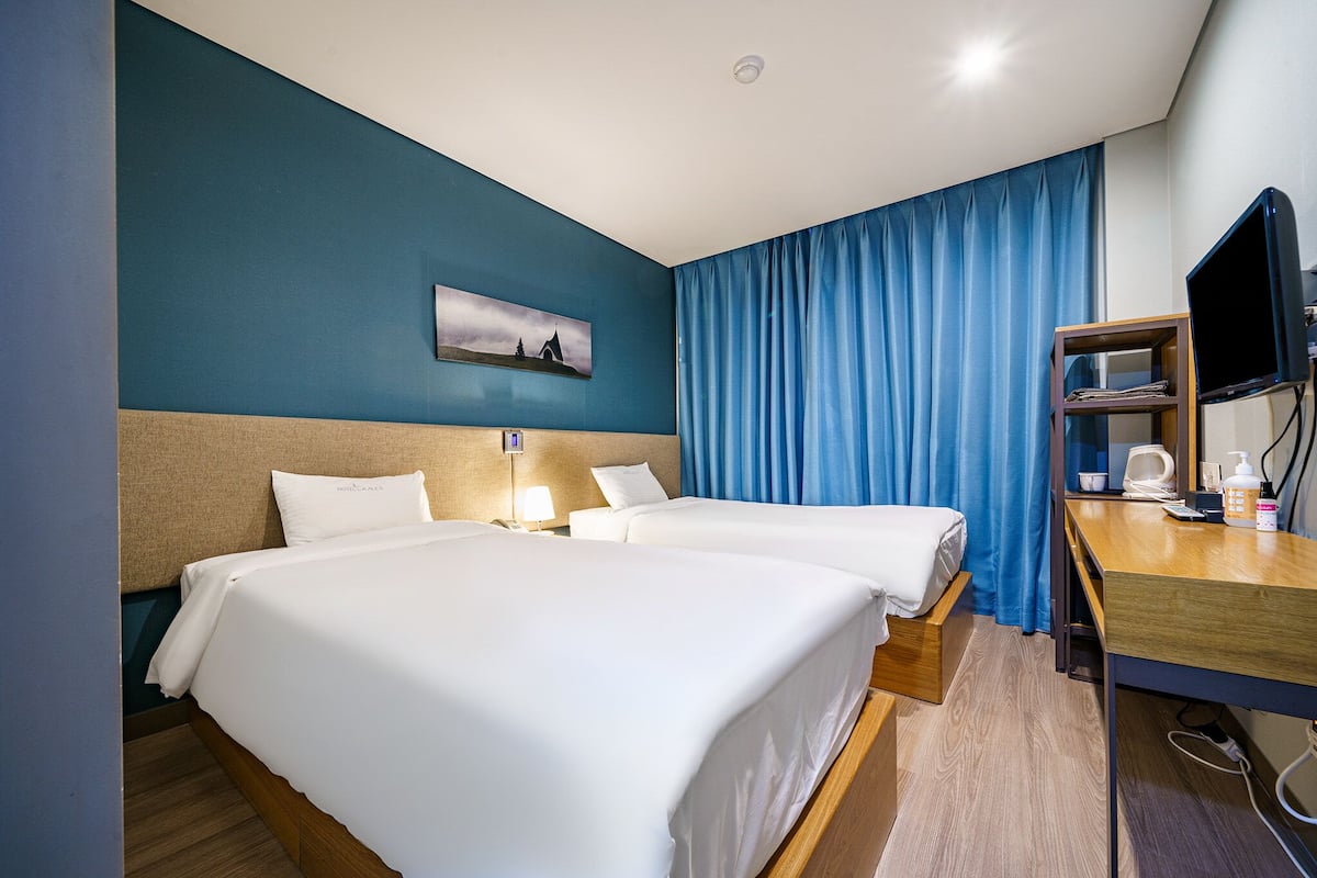 A hotel room with two beds, a desk, a television, and a painting on the wall.
