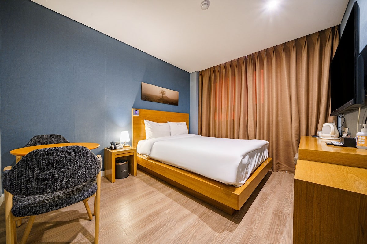 A hotel room with a bed, a desk, a chair, a TV, and a painting on the wall.