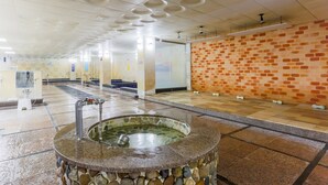 Un sauna public doté d’un bassin en pierre, de carrelages au sol et d’un mur décoré d’un motif en briques.