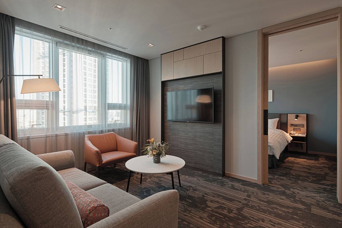 A modern hotel room with a sofa, armchair, round coffee table, and a bed.